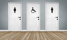 Drei Toilettentren nebeneinander, mit "Mann"-, "Frau"- und "Rollstuhl"-Piktogramm