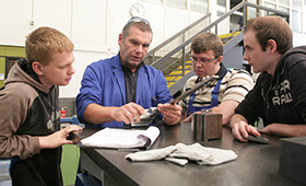 Ausbilder erklrt drei Auszubildenden ein technisches Werkzeug