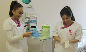 Zwei junge Frauen ziehen Latexhandschuhe an. Im Hintergrund Desinfektionsmittel.