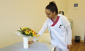 Eine junge Frau stellt eine Vase mit Blumen auf einen Tisch.