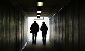 Zwei junge Menschen durchschreiten ein Tunnel, ihre Gestalten sind als Schattenrisse zu sehen