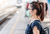 Junge Frau mit Mund-Nasen-Maske an einer S-Bahn-Haltestelle