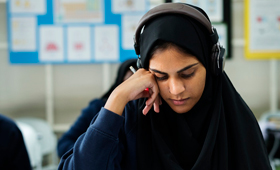 Junge Frau mit Kopftuch und Kopfhrer sitzt in einem Klassenraum und lernt