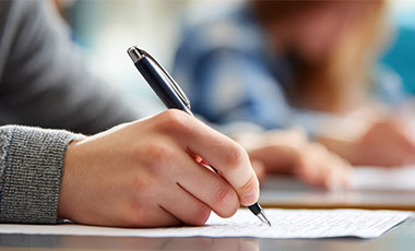 Man sieht eine Hand, die mit einem Stift auf Papier schreibt. Man sieht eine Hand, die mit einem Stift auf Papier schreibt.