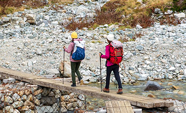 Zwei Frauen mit Wanderausrüstung überqueren eine improvisierte Brücke im Gebirge. Zwei Frauen mit Wanderausrüstung überqueren eine improvisierte Brücke im Gebirge.