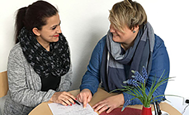 Zwei Frauen sitzen an einem Tisch und sprechen miteinander Zwei Frauen sitzen an einem Tisch und sprechen miteinander