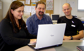 Eine Berufseinstiegsbegleiterin und zwei Lehrer blicken auf einen Laptop-Monitor