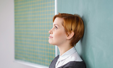 Junge Frau vor einer Schultafel schaut in Gedanken nach oben Junge Frau vor einer Schultafel schaut in Gedanken nach oben