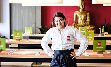 Eine junge Frau steht l�chelnd und in ihrer Arbeitskleidung als Servicekraft in einer Bar.