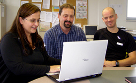 Eine Berufseinstiegsbegleiterin und zwei Lehrer blicken auf einen Laptop-Monitor