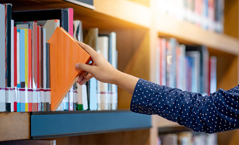 Ein Bücherregal in einer Bibliothek. Eine junge Frau greift nach einem orangefarbenem Buch. Ein Bücherregal in einer Bibliothek. Eine junge Frau greift nach einem orangefarbenem Buch.