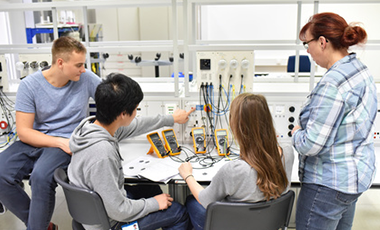 Das Bild zeigt vier junge an einem Tisch mit elektronischen Meßgeräten. Das Bild zeigt vier junge an einem Tisch mit elektronischen Meßgeräten.