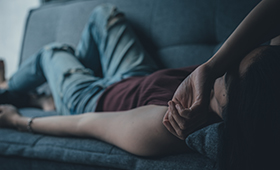 Junge Frau liegt auf einer Couch, einen Arm über die Augen gelegt Junge Frau liegt auf einer Couch, einen Arm über die Augen gelegt