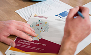 Zwei H�nde �ber ausgebreiteten Unterlagen der Servicestelle Jugendberufsagenturen, die auf einem Schreibtisch liegen