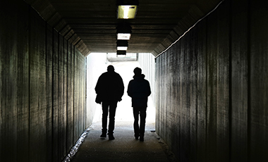 Zwei junge Menschen durchschreiten ein Tunnel, ihre Gestalten sind als Schattenrisse zu sehen