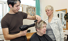 Auszubildender zum Friseurberuf mit Ausbilderin und Kundin
