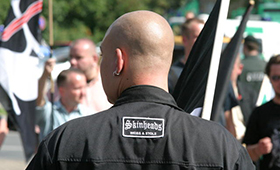 Skinhead von hinten, im Hintergrund eine Neonazi-Kundgebung