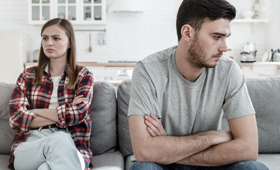 Eine junge Frau und ein junger Mann sitzen auf einer Couch und schauen in verschiedene Richtungen.