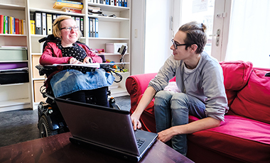 Ein Mann zeigt einer Frau im Rollstuhl etwas am Laptop