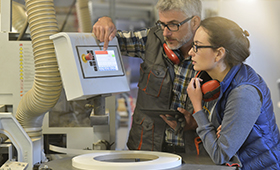 Ausbilder und Auszubildende vor einem Bildschirm in einem Produktionsbetrieb