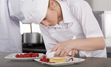 Auszubildende in Köchinnenkleidung stellt ein Dessert her Auszubildende in Köchinnenkleidung stellt ein Dessert her