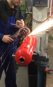 Ein Mann arbeitet mit einem Winkelschleifer an einem Metallbehälter, so dass die Funken stieben Ein Mann arbeitet mit einem Winkelschleifer an einem Metallbehälter, so dass die Funken stieben