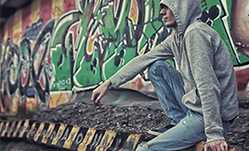 Junger Mann mit Kaputzenpullover vor Wand mit Graffitti.