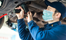 Auszubildender mit Mundschutzmaske bei der Autoreparatur