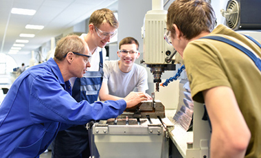 Auszubildende mit Ausbilder an einem Werktisch eines Betriebes Auszubildende mit Ausbilder an einem Werktisch eines Betriebes