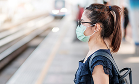 Junge Frau mit Mund-Nasen-Maske an einer S-Bahn-Haltestelle