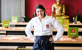 Eine junge Frau steht lächelnd und in ihrer Arbeitskleidung als Servicekraft in einer Bar