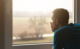 Junger Mann schaut aus dem Fenster in regnerische Landschaft.