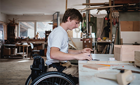Ein junger Mann im Rollstuhl arbeitet in einer Tischlerei