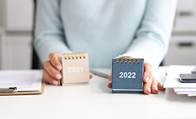 Am Schreibtisch sitzende Person tauscht Kalender 2021 gegen 2022