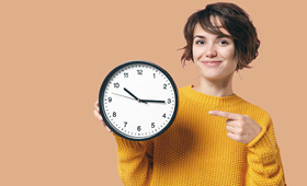 Junge Frau hlt eine Wanduhr in der Hand und zeigt lchelnd darauf