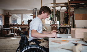 Junger Mann im Rollstuhl an der Werkbank einer Tischlerei