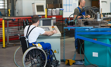 Junger Mann im Rollstuhl an einem Elektronikpult in einem Industriebetrieb Junger Mann im Rollstuhl an einem Elektronikpult in einem Industriebetrieb