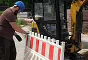 Baggerfahrer stellt neben seinem Bagger eine Baustellenabsperrung auf Baggerfahrer stellt neben seinem Bagger eine Baustellenabsperrung auf