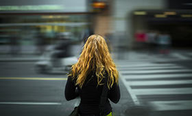 Junge Frau steht mit dem Rücken zum Betrachter vor einem Fußgängerüberweg