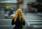 Junge Frau steht mit dem Rücken zum Betrachter vor einem Fußgängerüberweg