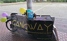 Ein Lastenrad mit Gangway-Banner lehnt an einem Laternenpfahl. Bild: Gangway