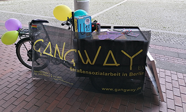 Ein Lastenrad mit Gangway-Banner lehnt an einem Laternenpfahl