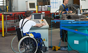 Mitarbeitender im Rollstuhl an einer Maschine in einer Produktionshalle