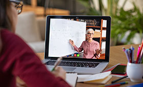 Frau schaut auf Laptop, der eine Frau mit Whiteboard zeigt