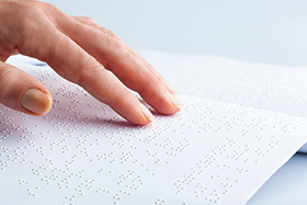 Finger ertasten eine Seite mit Braille-Schrift