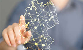 Eine durchsichtige Deutschlandkarte, ein Finger tippt eine Stadt an.