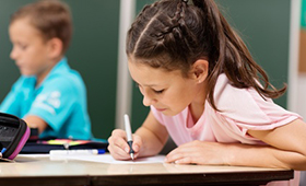 Ein Mädchen und ein Junge im Klassenraum einer Grundschule, im Hintergrund die Tafel