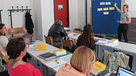 Eine Gruppe in einem Seminarraum. Die Dozentin zeigt etwas an einer Pinnwand. Bild: TH Kln