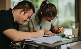 Junge mit Down-Syndrom und Mdchen im Rollstuhl lernen gemeinsam an einem Tisch