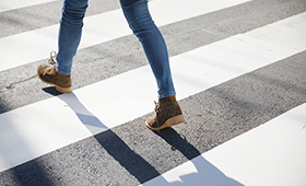 Beine eines jungen Menschen, in Jeans gekleidet, auf einem Zebrastreifen